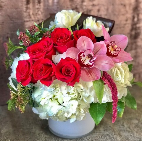 Red Roses, Pink Orchids, White Tulips arranged in a white glass vase.